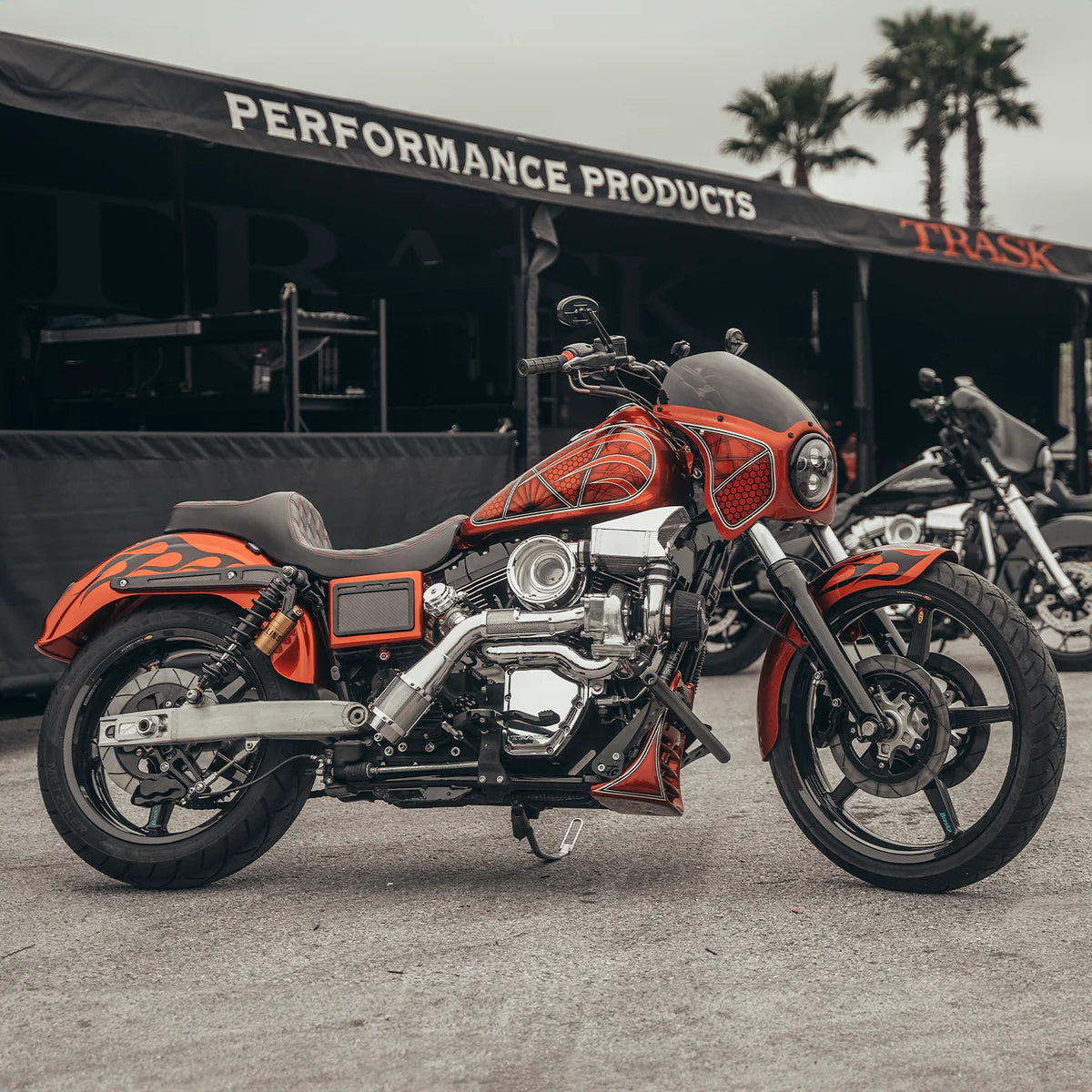 Wide angle shot of an orange Harley Davidson Dyna in front of the Trask Performance tent with Chrome Trask Dyna assault turbo kit installed on the bike